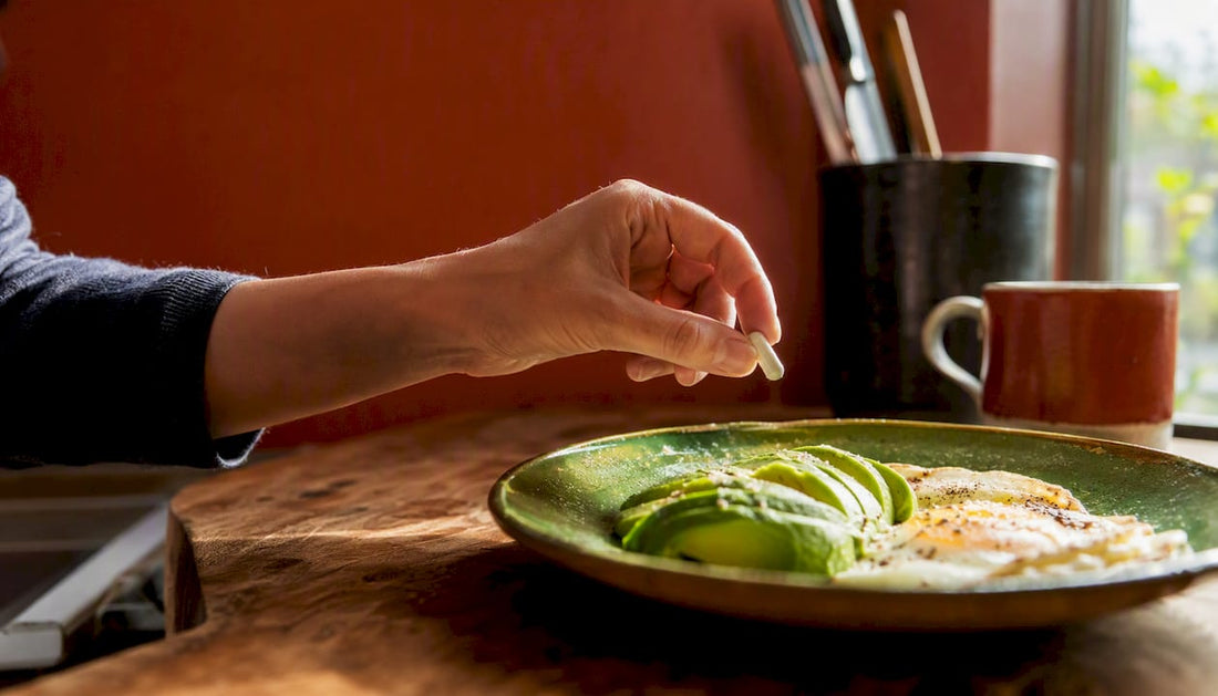 Hand picking probiotic capsule next to eggs and avocado